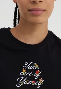 Black cotton t-shirt featuring white embroidered text "Take care of Yourself" with colorful floral accents around the words.