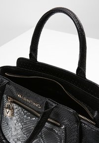 Svart texturerad läderhandväska med släta handtag, dragkedjefack och ett distinkt reptilmönster på det inre fodret.