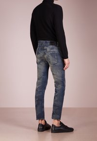 Smala jeans i blå denim med ett subtilt kamouflage-mönster, som har fem fickor och en svart läderpatch i midjan. Bärs med svarta sneakers.