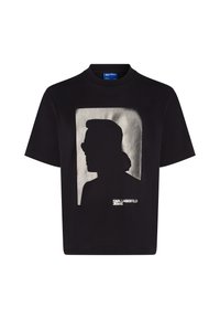 Melna T-kreklā ar baltu siluetu dizainu kvadrātā, zem grafikas ir teksts "KARL LAGERFELD JEANS". Īsas piedurknes, apaļa kakla izgriezums.