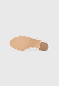 White strappy sandal with a smooth, open toe design, beige rubber outsole, and textured sole for grip.