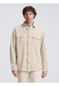 Beige overhemd met knoopsluiting van lichtgewicht stof, met twee borstzakken, een klassieke kraag en zichtbare knoopdetails.