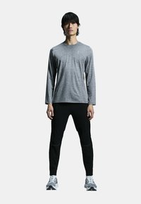 Grå langærmet skjorte med rund halsudskæring, kombineret med sorte tapered bukser med lynlåslommer, og lysegrå sportssko.