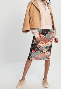 Skórzana kurtka w kolorze brązowym, jasnoszara bluzka z polaru, midi spódnica w kwiatowy wzór z czarnymi i kolorowymi akcentami oraz jasne trampki.