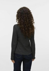 Langsleeve zwart gestreept shirt met dunne witte lijnen, aangesloten vorm, gemaakt van katoen, gecombineerd met donkerdenim jeans.