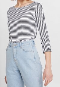 Randig långärmad tröja i svart och vitt, kombinerad med ljusblå högmidjade jeans. Toppen har rund halsringning och en figurnära design.