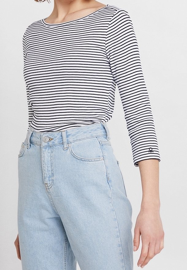 Randig långärmad tröja i svart och vitt, kombinerad med ljusblå högmidjade jeans. Toppen har rund halsringning och en figurnära design.