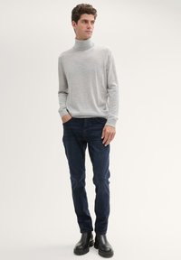 Maglione a collo alto grigio chiaro realizzato in tessuto morbido, abbinato a jeans blu scuro e stivaletti neri, con una vestibilità comoda e maniche lunghe.