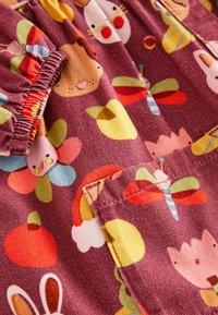Tissu bordeaux présentant des motifs animaliers et floraux colorés de style cartoon. Comprend des bords froncés et un détail de poche avec une texture lisse.