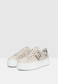 Beige lædersneakers med en kraftig hvid sål, der har metalliske detaljer, snørebåndsdesign og dekorativt sidehardware.