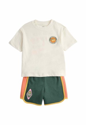 Cream short-sleeve top with "Fresh Orange Juice" patch paired with green shorts featuring pink side panels and yellow trim, and an "Island Goods" patch.