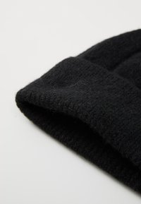 Beanie negru tricotat, cu o suprafață moale și texturată, și cu o margine pliată. Materialul pare călduros și flexibil, cu o ușoară pufosenie vizibilă.