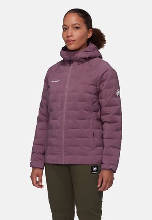 Giacca a vento viola con cappuccio, dotata di zip frontale e texture trapuntata. Logo sul petto e un distintivo sulla manica. I pantaloni sono di colore verde oliva.