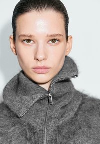 Maglione grigio con zip, collo alto e texture morbida. Presenta una cerniera argento ed è realizzato in un materiale soffice.
