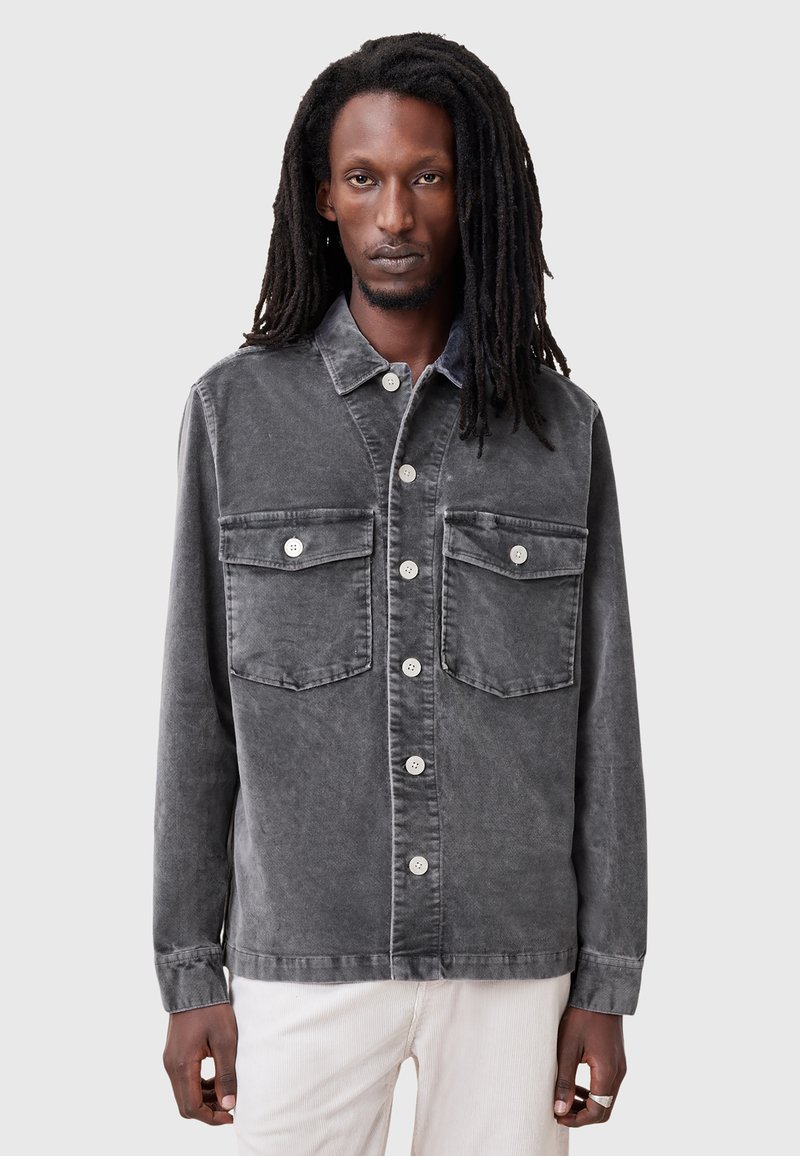 Camisa de mezclilla gris con cierre de botones en la parte delantera, dos bolsillos en el pecho y un corte relajado. Presenta botones blancos a contraste y una textura suave.