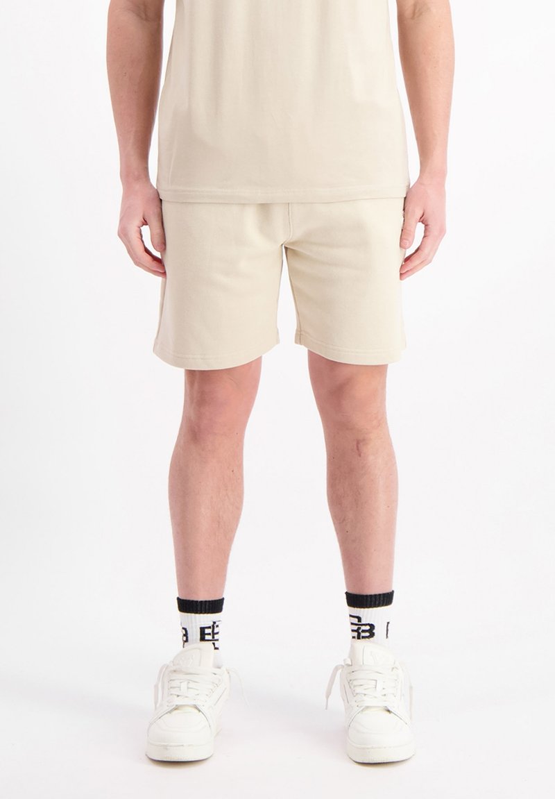 Beige katoenen shorts met een ontspannen pasvorm, met een gladde textuur en gestikte details, gecombineerd met witte sneakers en sokken met zwarte accenten.