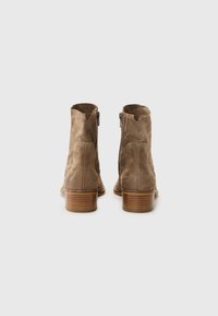 Botas de ante marrón hasta el tobillo con un borde superior en forma de ondas y cremalleras laterales, con un tacón de madera apilada y textura suave.