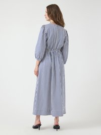 Striped dress with blue and white vertical lines, cinched waist, and puffed sleeves. Flowy fabric and ankle-length cut. Black heels.