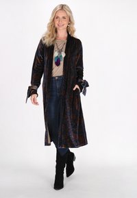 Lange fluwelen jas in donkerblauw met een paisleypatroon, voorzien van strikmanchetten en een open voorkant. Draag het over een beige top en combineer het met blauwe jeans.