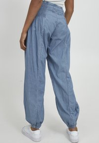 Pantalones de mezclilla sueltos de color azul claro con una cinturilla fruncida y puños elásticos. Combinados con zapatillas blancas.