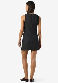 Bezgali piedurkņu tumšs džinsu kleita ar taisnu piegriezumu, aizmugurēju rāvējslēdzēju un minimāliem šuvju lielumiem. Valkāta ar tumšām slip-on apaviem.