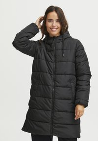 Giacca a vento nera imbottita con cappuccio, caratterizzata da un design trapuntato, chiusura con zip e tasche laterali. Realizzata in materiale leggero e resistente all'acqua.
