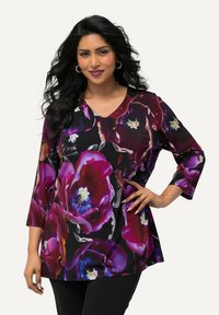 Lila tunika mit floralem Muster, V-Ausschnitt und dreiviertel Ärmeln. Hergestellt aus leichtem Stoff, mit großen Blüten auf schwarzem Hintergrund.