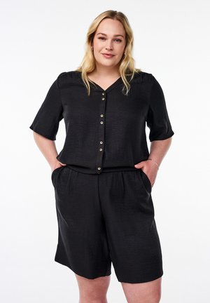 Jumpsuit nero a maniche corte con scollatura a V, caratterizzato da una fila di bottoni dorati, tessuto texturizzato e tasche laterali. Vita elasticizzata.