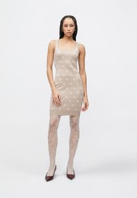 Bēšas krāsas adīta kleita ar smalku rombu rakstu; kopā ar caurspīdīgām rakstainām zeķubiksēm un bordo krāsas apaviem ar smailiem pirkstgaliem.