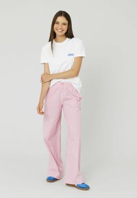 T-shirt blanc avec du texte bleu indiquant "Freshly Squeezed", associé à un pantalon large rayé rose et blanc et des chaussures plates bleues.