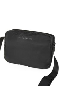 Bandolera negra con una superficie lisa y acolchada, que presenta un cierre de cremallera y una correa ajustable. Logo grabado en la parte frontal.
