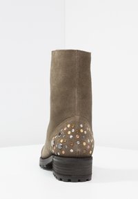 Zelené semišové kotníkové boty s texturovaným povrchem, zaoblenou špičkou a masivním černým podpatkem. Na zadní části se nachází různé kovové nýty v zlaté, stříbrné a měd�ěné barvě.