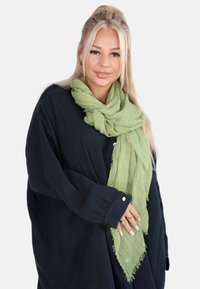 Light green textured scarf with frayed edges worn over a loose black shirt. The material appears soft and airy, suitable for layering.
