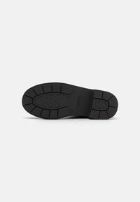 Suela de zapato de goma negra con un patrón de agarre texturizado y un arco moldeado. Presenta un diseño robusto y segmentado para estabilidad y tracción.