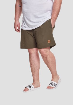 Mørke olivengrønne shorts lavet af letvægtsstof, med sidelommer og et lille struktureret logo-patch. Båret med hvide slidesandal.
