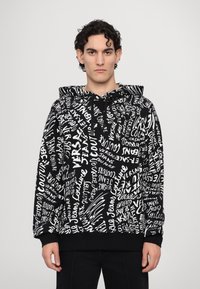 Haut à capuche noir avec des motifs en texte blanc. Comprend une capuche avec cordons, des manches longues et une taille ajustée. Fabriqué en tissu doux.