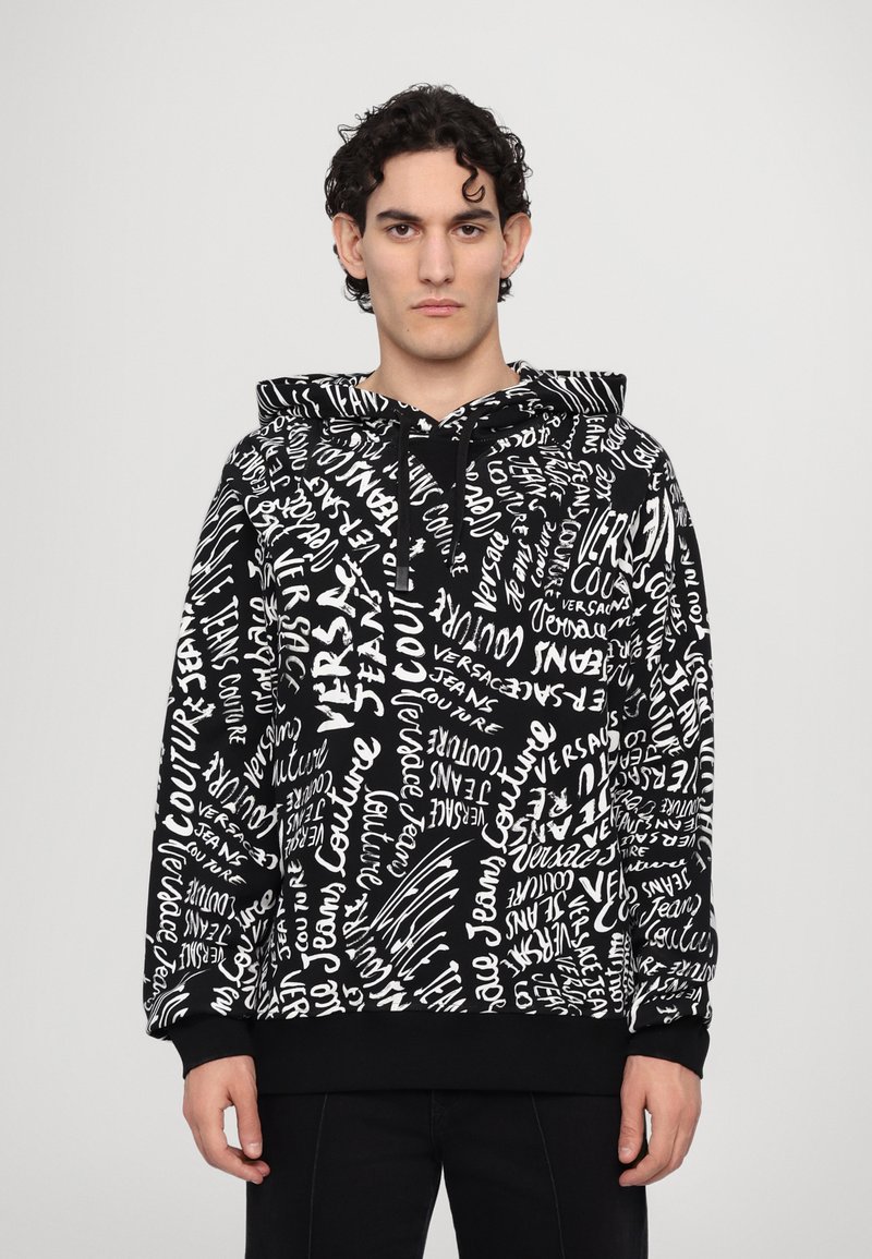 Haut à capuche noir avec des motifs en texte blanc. Comprend une capuche avec cordons, des manches longues et une taille ajustée. Fabriqué en tissu doux.