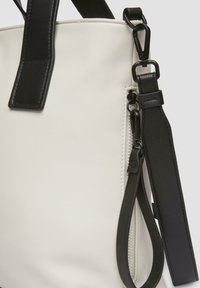 Biała syntetyczna torba tote z czarnymi skórzanymi akcentami, górnymi uchwytami i bocznym zamkiem. Posiada teksturowane materiały i regulowany pasek.
