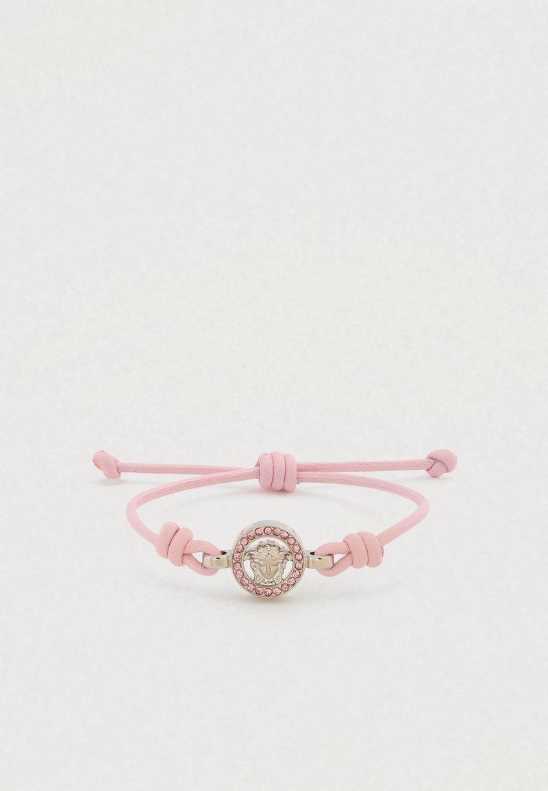 Rožinės odos apyrankė su apvaliu metaliniu pakabuku, vaizduojančiu liūto galvą ir rožinių akutėlių apvadu. Reguliuojamas raištelių užsegimas.