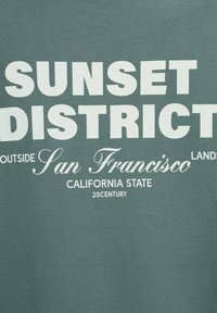 T-shirt in cotone verde con testo bianco in grassetto: "SUNSET DISTRICT," "San Francisco," e "CALIFORNIA STATE 20CENTURY." Texture liscia.