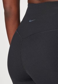 Crne rebraste tajice imaju visoki pojas i diskretni Nike logotip na leđima, ističući elegantan i prilagođen dizajn.