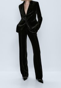 Costume en velours noir comprenant un blazer ajusté à encolure profonde et un pantalon taille haute assorti à coupe droite.