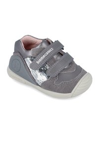 Zapatilla gris para niño pequeño con parte superior de ante y lentejuelas. Cuenta con dos tiras de velcro y una suela de goma con detalles texturizados.
