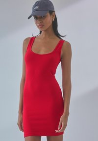 Abito a tubino rosso rigato con scollo a barca e design aderente. La modella indossa un berretto scuro con la scritta "self." ricamata sul davanti.