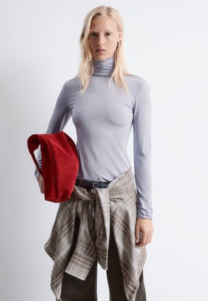 Lila langärmliges Oberteil, rote Wildledertasche und gewickeltes braunes Karoshemd, kombiniert mit dunklen Hosen. Glatter Stoff und weiche Texturen.