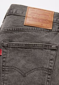 Bolsillo trasero de unos vaqueros Levi's grises con parche de cuero marrón de la marca y etiqueta de tela roja de Levi's en la costura lateral.
