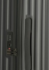 Valise rigide noire avec une texture striée, double fermeture éclair avec verrou à combinaison et une poignée de marque.