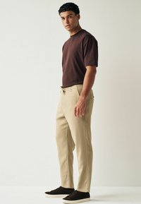 Pantalons beiges avec une coupe décontractée et une taille à cordon, associés à une chemise marron à manches courtes. Des baskets sombres complètent le look.