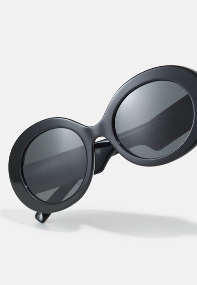 Čierne oversized slnečné okuliare s okrúhlymi rámami a tmavými sklami. Hladký matný povrch so slabým leskom na sklách. Pevné nožičky.