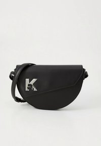 Črna usnjena torbica čez ramo s ukrivljeno obliko. Ima srebrn logotip "K" in teksturiran diagonalni poudarek. Priložen je nastavljiv trak.
